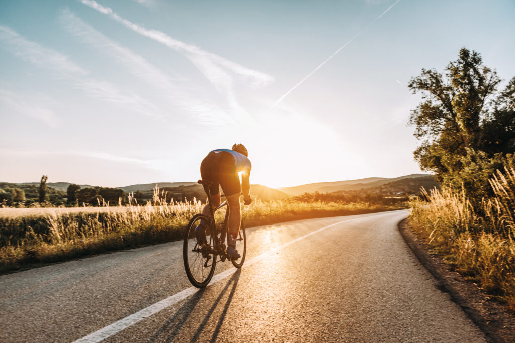 Rennradfahrer auf Landstraße bei bestem Wetter und untergehender Sonne.